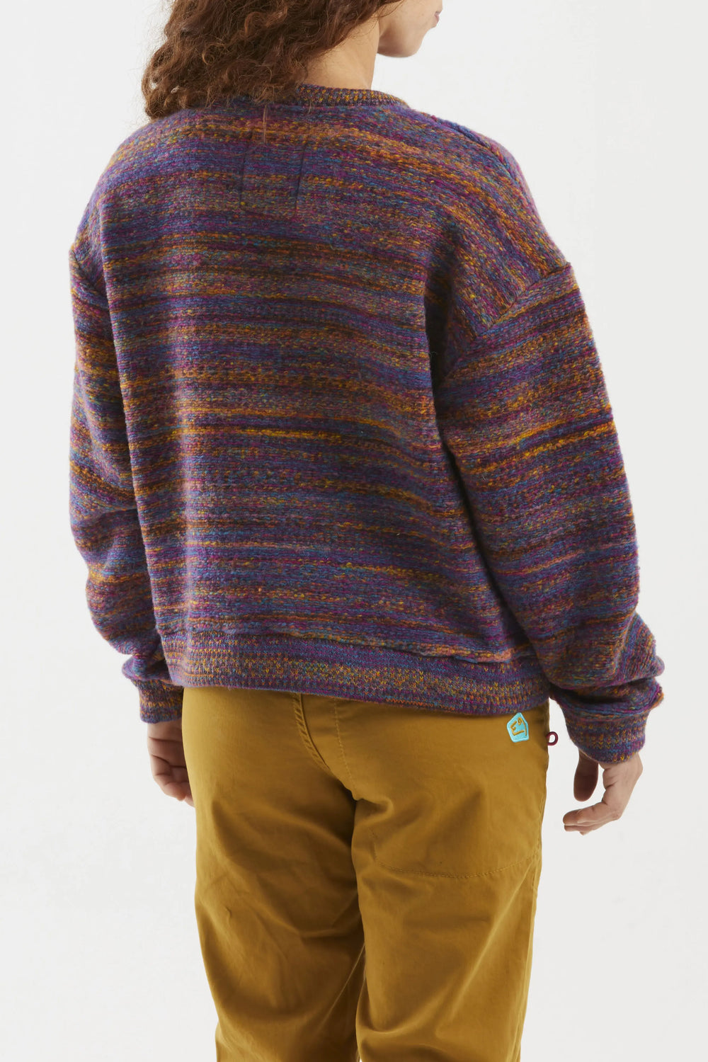 Person wearing a patterned wool sweater and brown pants on a white background