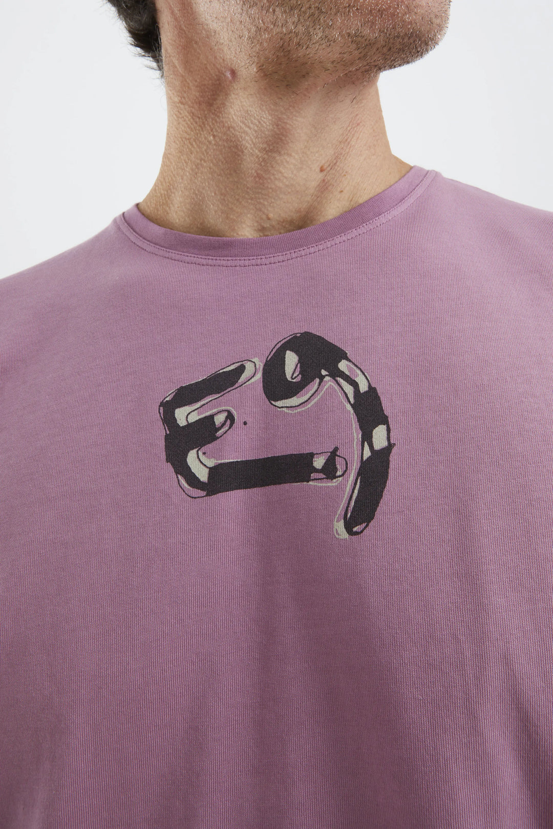 Person wearing a purple t-shirt with a black logo on a plain background